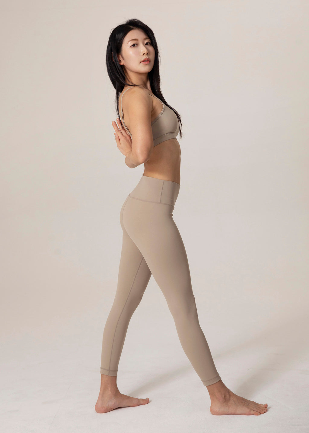 Side view of model standing in beige Flowmango Inner Flow leggings with matching bra