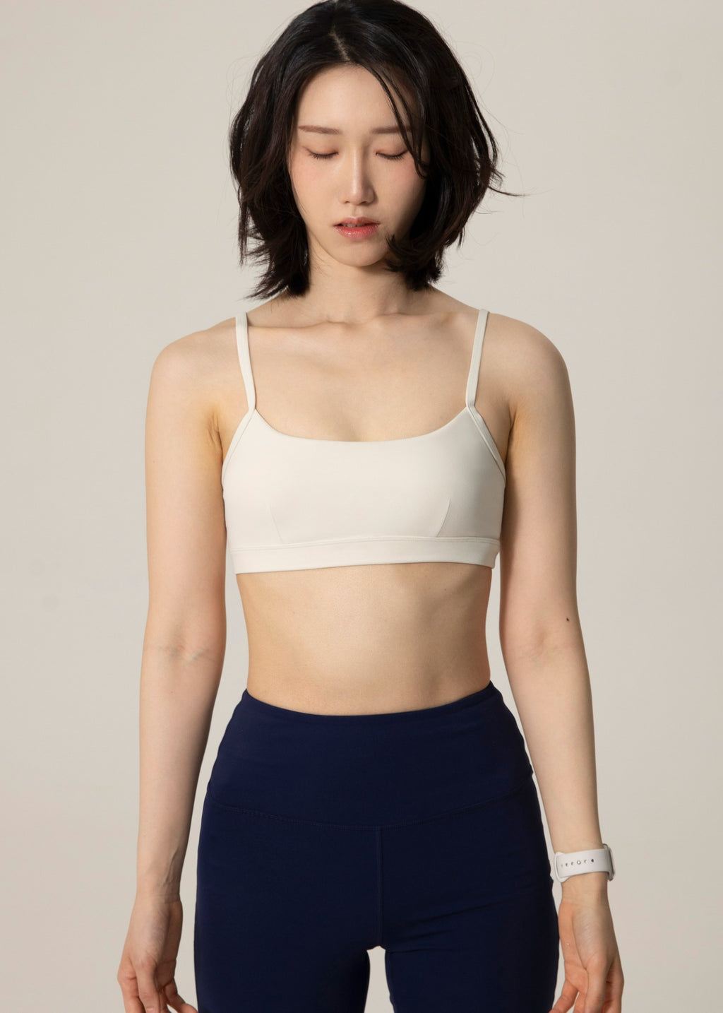 Front view of model wearing ivory Flowmango Inner Flow bra and navy leggings while looking down