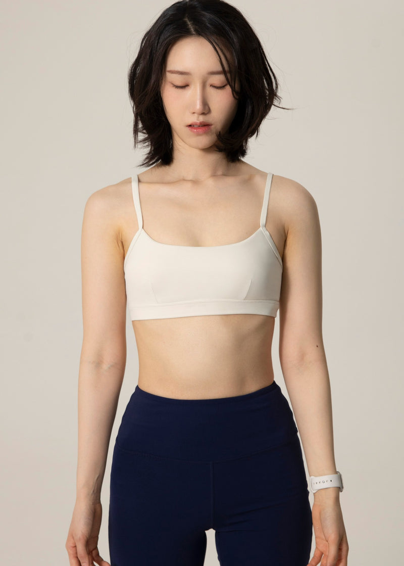 Front view of model wearing ivory Flowmango Inner Flow bra and navy leggings while looking down