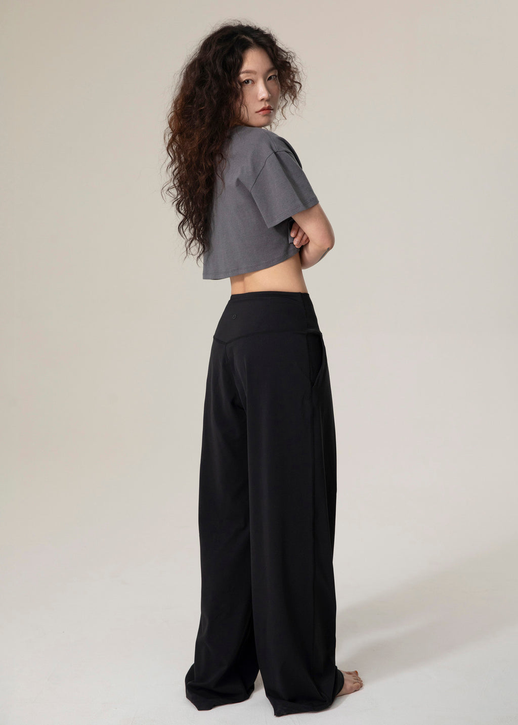 Back and side view of model wearing black Flowmango Deep Flow wide-leg pants with a charcoal cropped top