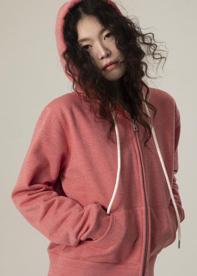 Front view of model in the dusty rose Dot Flow zip-up hoodie with hood up and hands in the front pockets