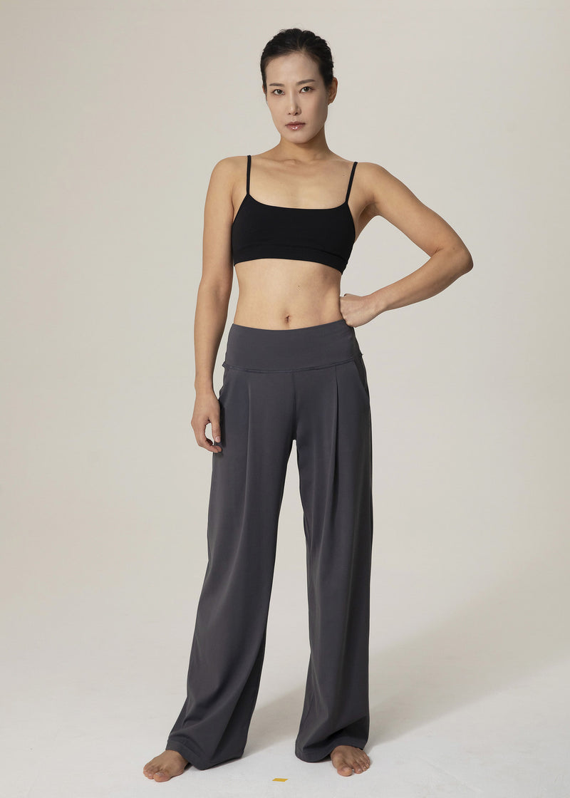 Front view of model wearing slate gray Flowmango Deep Flow wide-leg pants and black sports bra with one hand on hip