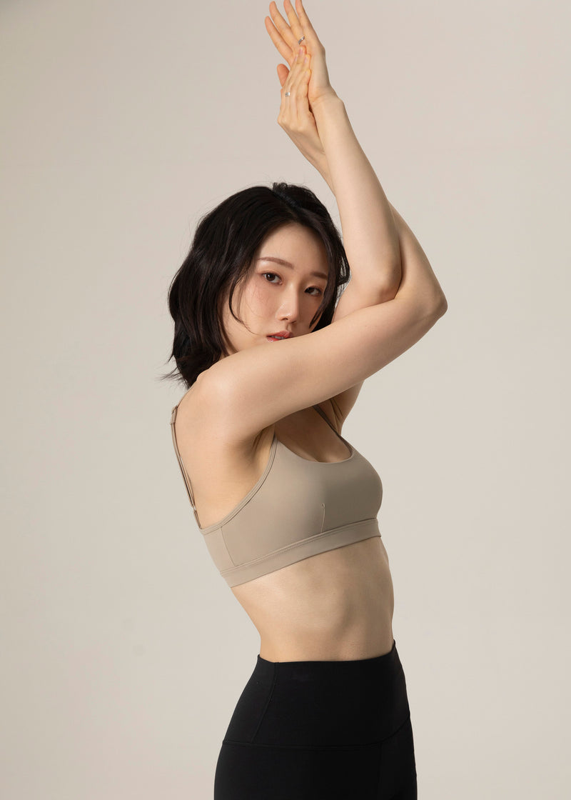 Side view of model in beige Flowmango Inner Flow bra and black leggings with one arm raised