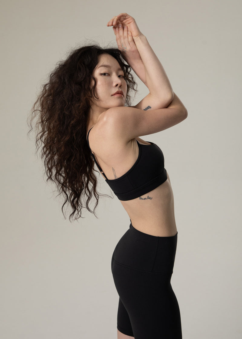 Back and side view of model wearing black Flowmango Inner Flow bra with one arm raised
