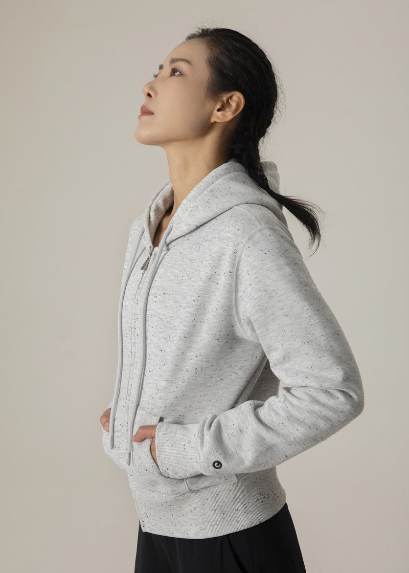 Side profile of model wearing the heather gray Dot Flow zip-up hoodie with hood down and hands in pockets