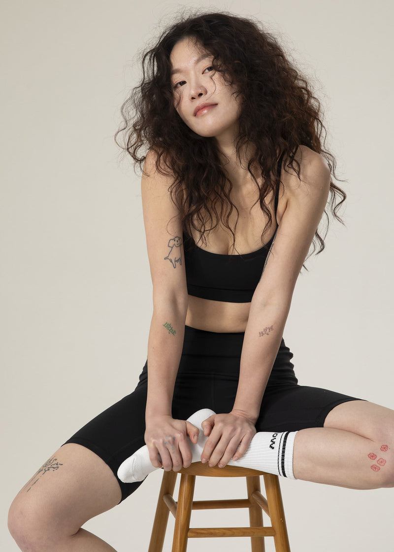 Model seated on a stool in black activewear wearing white Flowmango crew socks