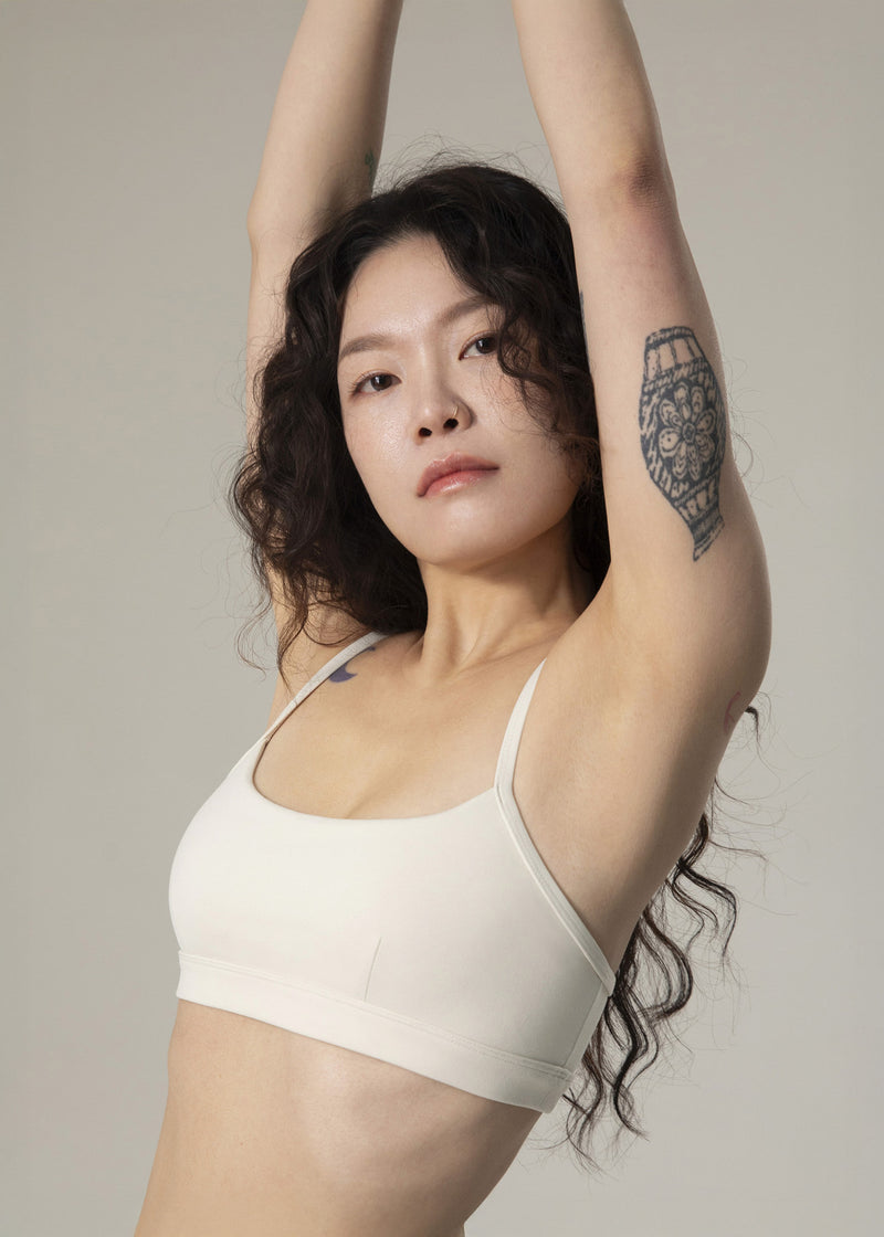 Close-up of model in ivory Flowmango Inner Flow bra stretching both arms overhead