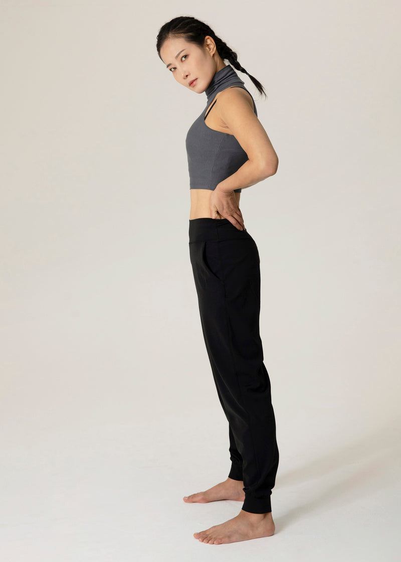 Side view of model standing in black Flowmango jogger pants with a hand at the waistband