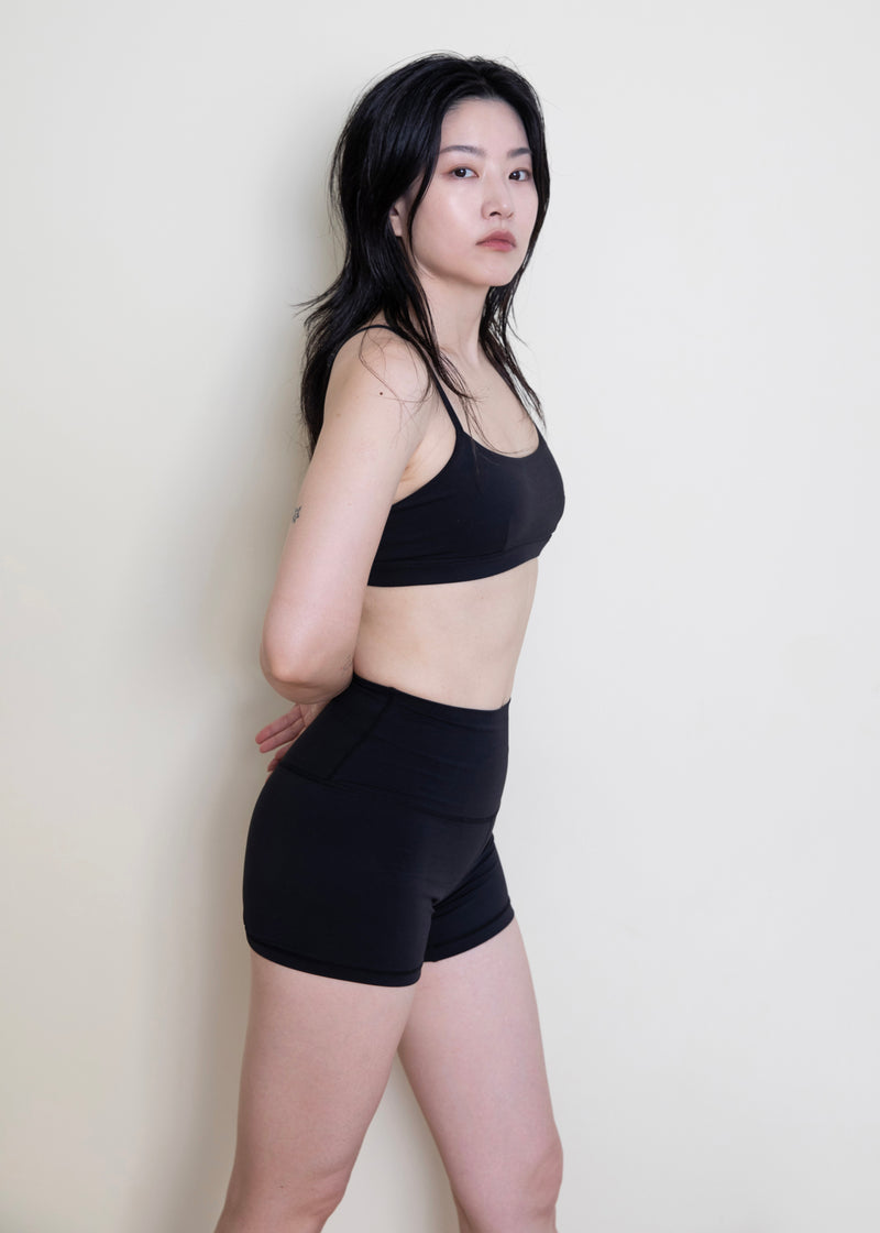 Model standing in black Deep Flow Shorts and a matching activewear bra, three-quarter view