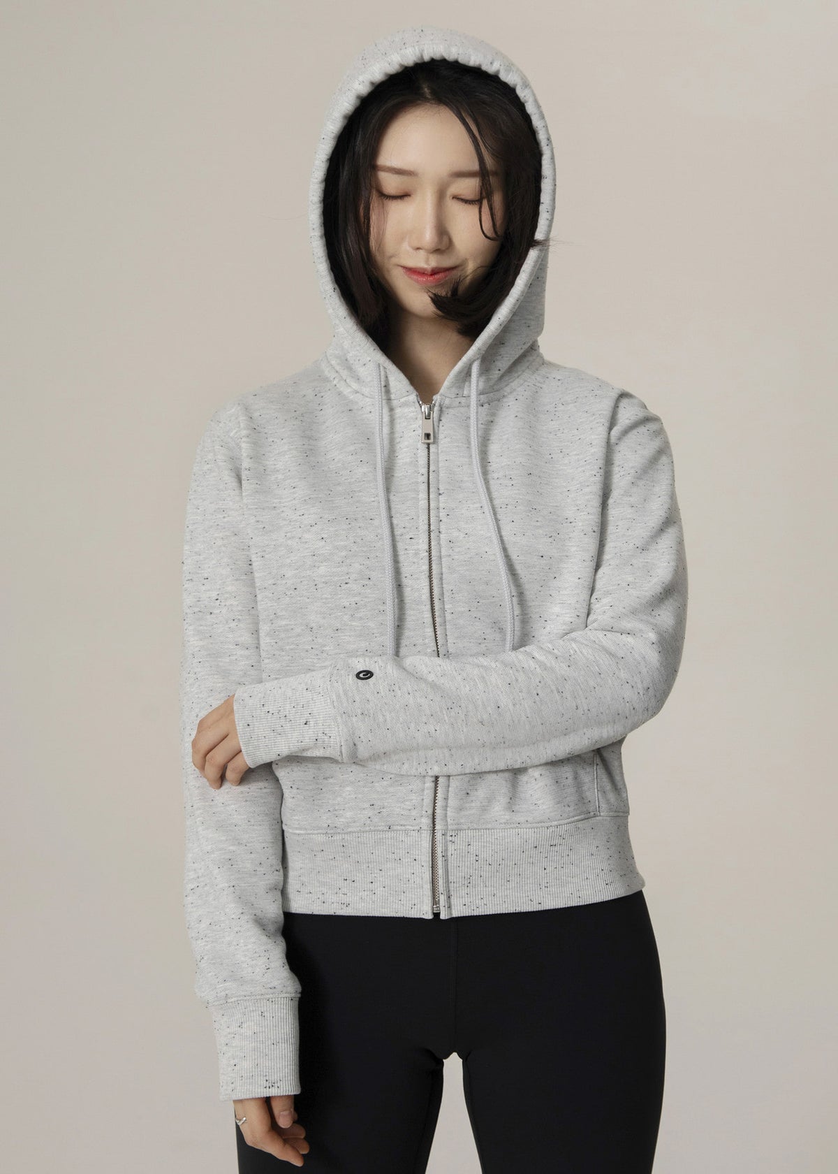 Front view of model wearing the zipped heather gray Dot Flow hoodie with hood up and black leggings
