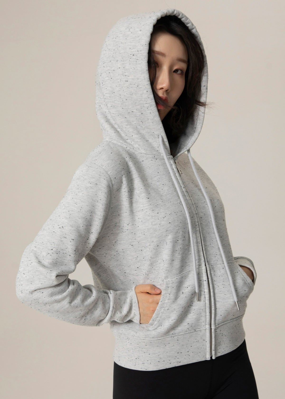Model wearing the heather gray Dot Flow zip-up hoodie with hood up and hands in the front pockets