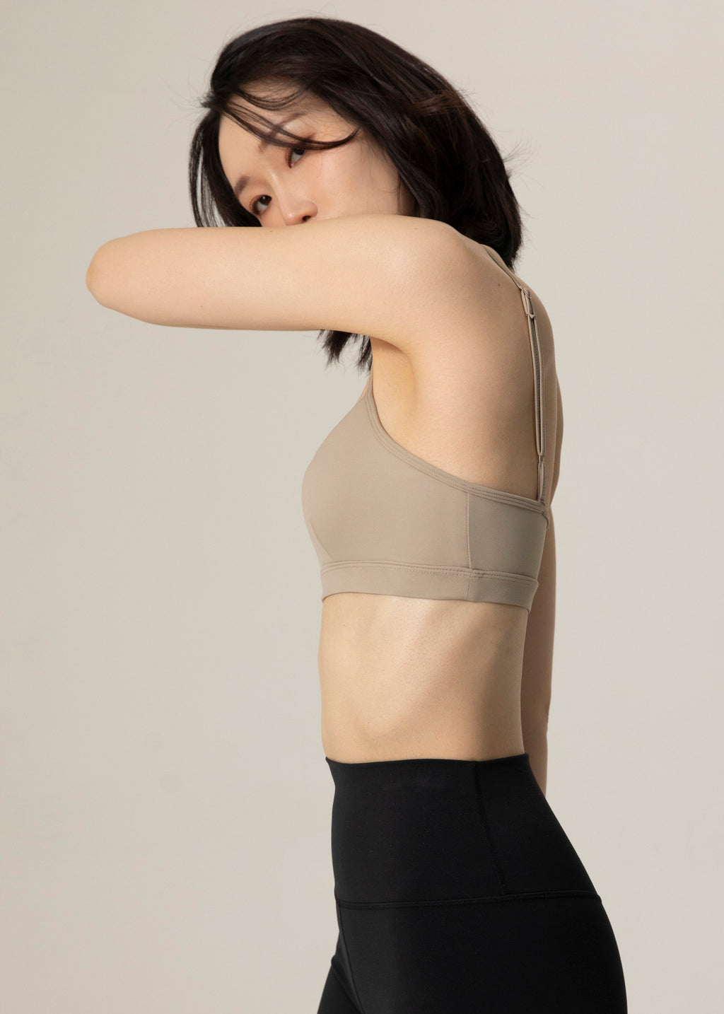 Rear three-quarter view of model in beige Flowmango Inner Flow bra and black leggings with one arm bent