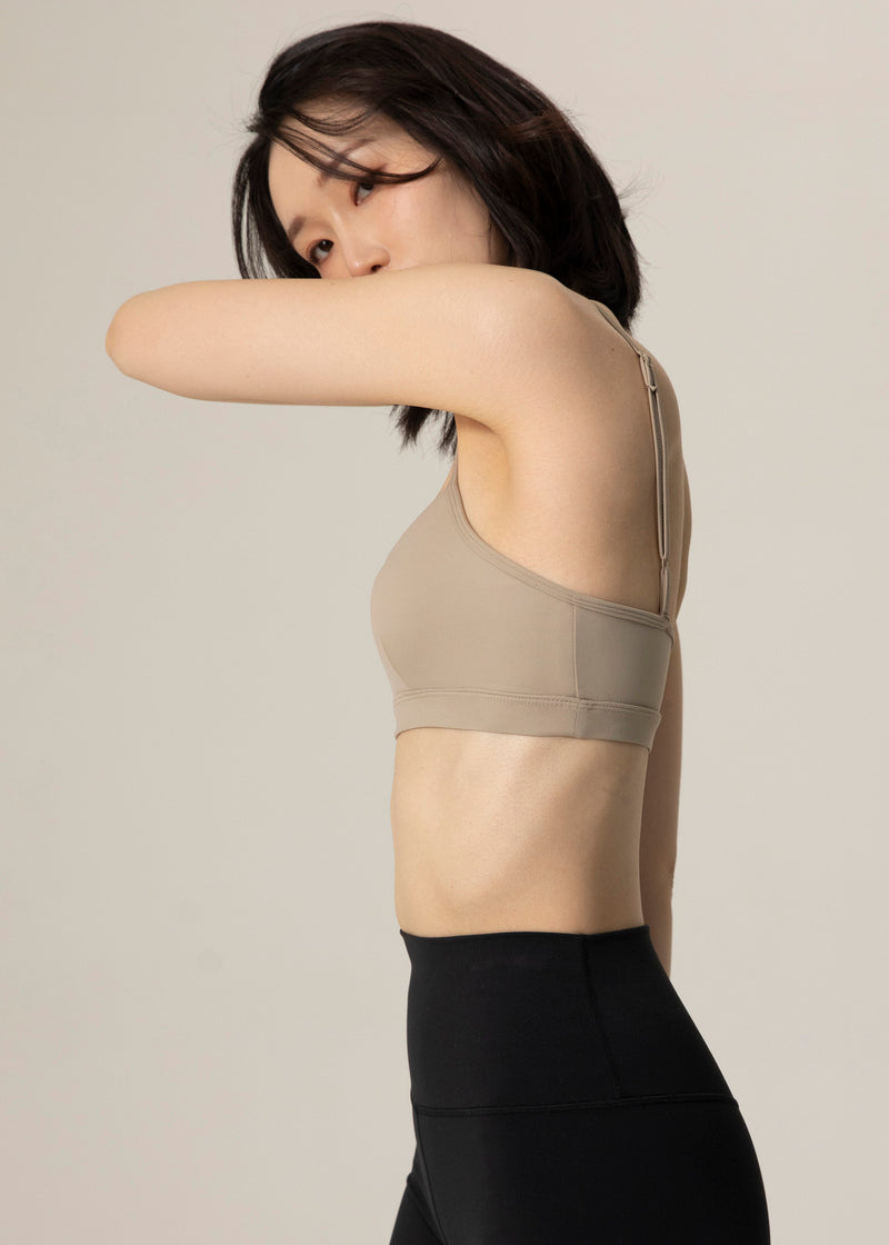 Rear three-quarter view of model in beige Flowmango Inner Flow bra and black leggings with one arm bent