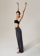 Side view of model in slate gray Flowmango Deep Flow wide-leg pants and black sports bra with arms raised