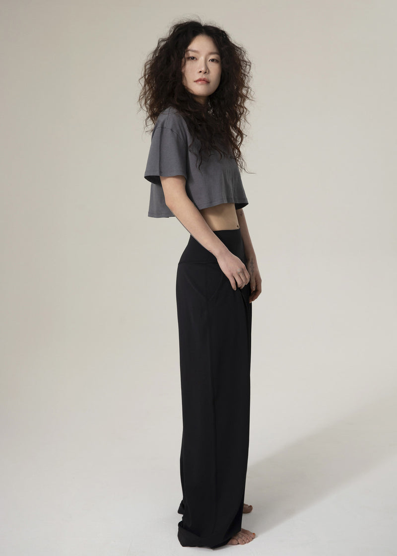 Side view of model standing in black Flowmango Deep Flow wide-leg pants and charcoal cropped top